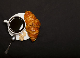 Croissant and cup of coffee on black background