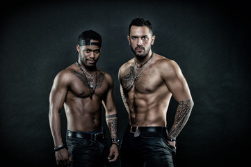 Fototapeta na wymiar Machos with muscular tattooed torsos look attractive, dark background. Guys sportsmen with sexy muscular torsos. Masculinity concept. Athletes on confident faces with nude muscular chests