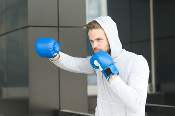 Man athlete on concentrated face with sport gloves practicing boxing punch, urban background....