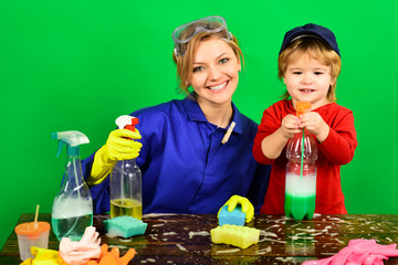 Boy holds spray on table. Smiling woman sit at wooden table with cleaning products. Cleaning activities concept. Cute little helper. Cleaning concept. Cleaning service and work concept.