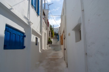 Fototapeta premium Street with steps in Mykonos, Greece. Whitewashed houses with blue wooden shutters architecture. Summer vacation on mediterranean island. Traveling and wanderlust. Famous tourist destination