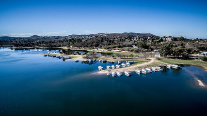 Vista aérea de un lago azul, con embarcaciones y de fondo montañas y un cielo azul
