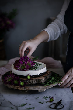 Close up of a woman's hand garnishing cake with flowers