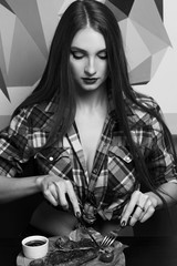 Gorgeous seductive woman dressed in unbuttoned checkered shirt sitting at table and eating delicious steak with knife and fork. Young beautiful female model at steakhouse or meat restaurant.