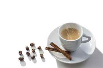 White steamy cup near cinnamon sticks in coffee beans, whitebackground