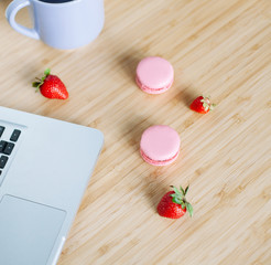 Workplace with laptop,  macaroons, strawberry and cup of tea