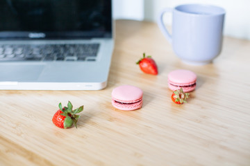 Workplace with laptop,  macaroons, strawberry and cup of tea