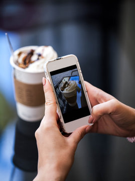 Closeup of women's hands making photo of sweet dessert on mobile phone while sitting in comfortable restaurant, female taking pictures with cell phone camera