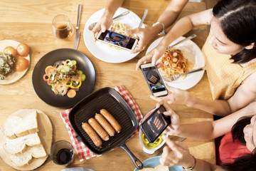 Enjoy dinner eating party blogger  with friends and taking photo by phone to post into social networks, top view of foods on table and group of funny and delicious people