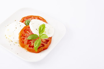 Mozzarella and tomatoes with basil on a white square plate. The background is white. Copiespice.