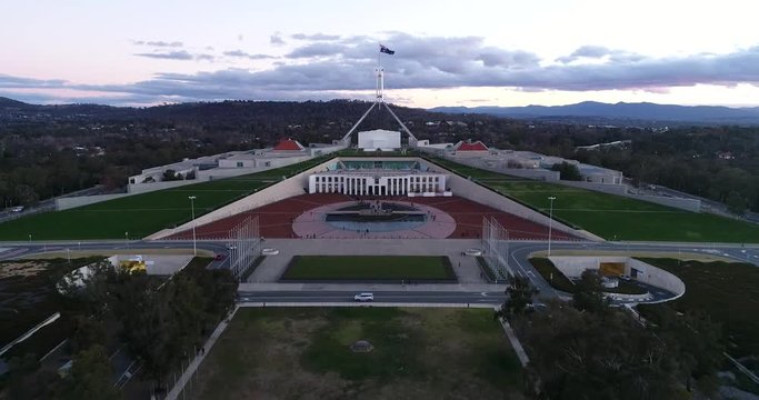 Close to parliament house on capitol hill in Canberra surrounded by grass lawns, gum trees in park and roads at sunset.
