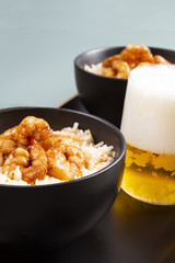 Fried shrimp and rice in a black bowl. Glass with beer. The background is gray.