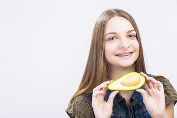 Dental Health Concepts. Positive caucasian Teenager Girl Wearing Teeth Braces Posing with Avocado Against White.