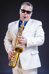Fototapeta premium Music Themes and Ideas. Tranquil Caucasian Mature Saxophonist Against Black Background.