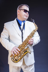 Dreaming Male Saxophonist Posing In Sunglasses With Sax. Against Black Background.