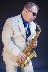 Fototapeta na wymiar Portrait of Expressive Mature Playing Saxophonist Posing In Sunglasses With Sax. Against Black Background.