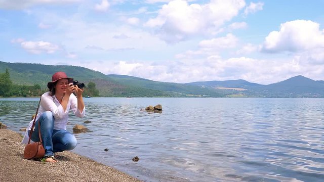 Happy beautiful woman hobby photographer taking pictures of nature in front of sea and mountains