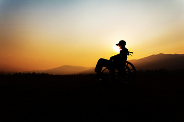 Silhouette of disabled person in a wheelchair on the sunset background,