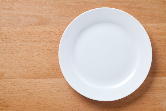 Empty white plate on wooden table. Top view.