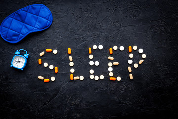 Obraz premium Medicine helps get asleep. Good sleep. Word sleep lined with sleeping pills near sleeping mask and alarm clock on black background top view copy space