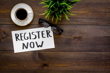 Membership concept. Template for registration. Register now hand lettering iconon word desk with glasses, coffee, plant on dark wooden background top view space for text