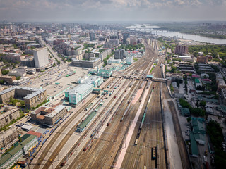 Obraz premium Aerial photography of a modern railroad tracks, trains with wagons on parallel railways, crossings, a railway station, high-rise buildings, a bridge across the river on a warm summer day. 