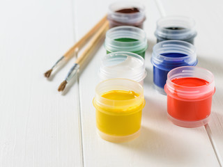 Open jars of gouache and brushes on a white wooden table. Creative kit.