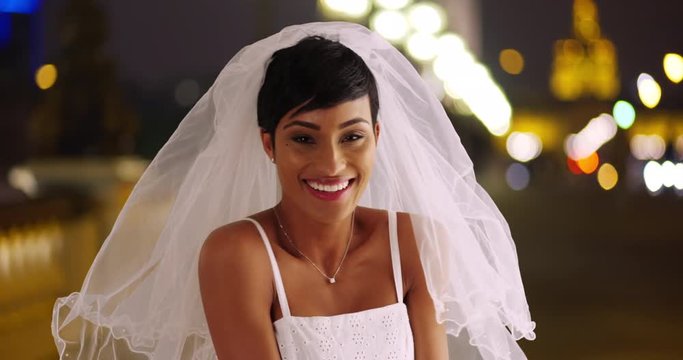 Happy beautiful bride outside at night laughing and excited, Black woman in her wedding dress lifts away veil, 4k