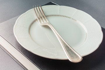 White plate with a fork lies on a thick black book