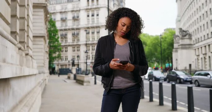 Pretty black woman standing on city street checking her phone, African American female answering text message from friend, 4k