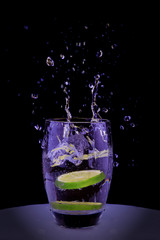  A slice of lime falls into a glass, sprays fly in all directions