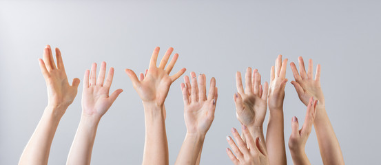 Many women's hands raised up on a gray background.