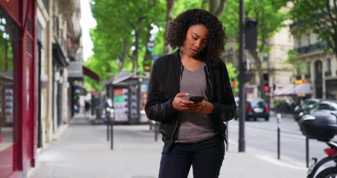 Pretty black woman standing on urban street using cellphone, Portrait of a woman checking her phone for new texts, 4k