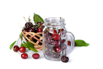 Cherries in a basket and a glass jar on a white isolated background.