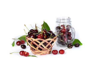 A basket of cherries in the foreground and a jar of cherries in the background.