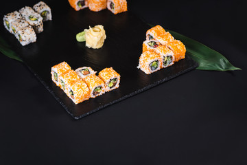 A set of different sushi rolls with caviar on black background