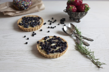 Blueberry tart on white wooden table; culinary concept; selective focus background.