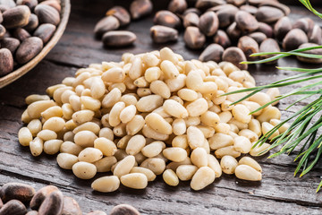 Pine nuts in the spoon and pine nut cone on the wooden table. Organic food.