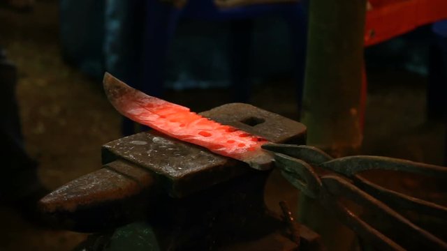 blacksmith manually forging hot metal knife on anvil in traditional