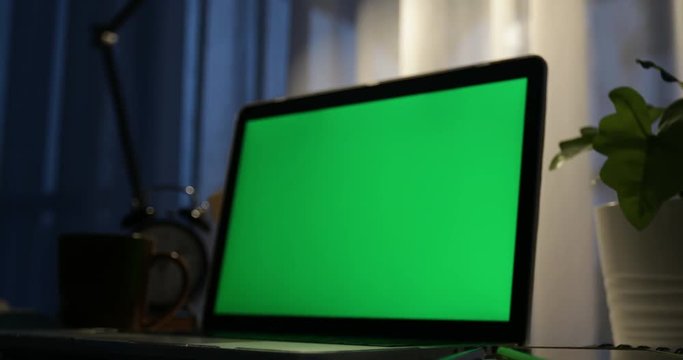 Laptop with green screen. Dark office. Dolly in . Perfect to put your own image or video.Green screen of technology being used. Chroma Key laptop