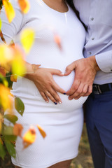 close up view of loving couple makes heart from fingers on the tummy of a pregnant girl