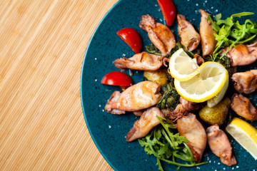 Grilled squid with lemon and vegetables on color plate at Italian restaurant