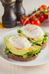 Avocado toast, cherry tomato and poached eggs on wooden background. Breakfast with vegetarian food, healthy diet concept.