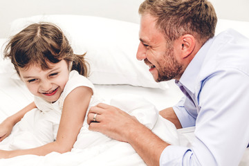 Obraz premium Father with little daughter having fun and playing together on the bed at home.Love of family and father day concept