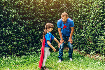 Father with little daughter in superhero costume having fun and playing superheroes together at park outdoors.Love of family and father day concept