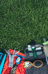 Fototapeta premium Set of equipment for hiking and travel on green grass with copy space . Items include , multi tool, flashlight, hygiene products, tracking clothes, comb