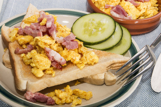 scrambled eggs with fried bacon, toasted bread and sliced cucumber