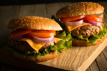 Home made hamburger with beef, onion, tomato, lettuce and cheese. Fresh burger close up on wooden rustic table with potato fries, beer and chips. Cheeseburger.