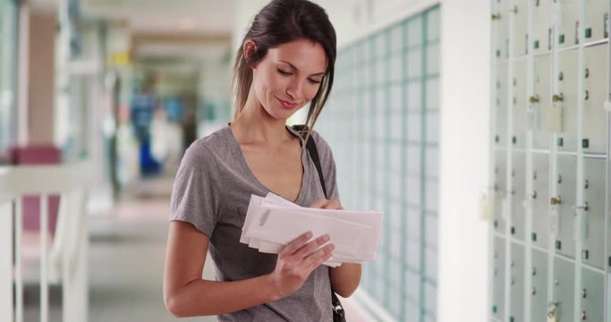 Young Caucasian woman looking through mail she received while at post office, White millennial female checking stack of letters while in post office hallway, 4k