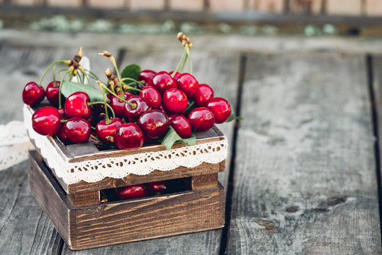 Cherries with leaves in vintage wooden box on rustic wooden table. Copy space